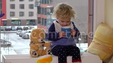 可爱的孩子喝茶，和玩具熊一起坐在靠近窗户的加热器上